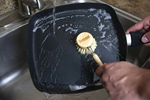 Person cleaning a square pan in a sink with a brush.