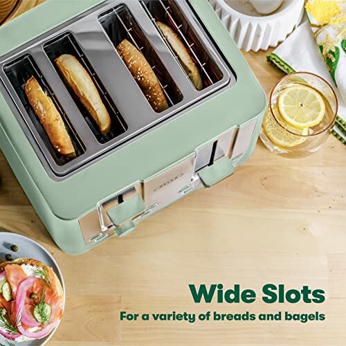 Green toaster with wide slots and bagels inside, next to a plate of salmon and a lemon drink.